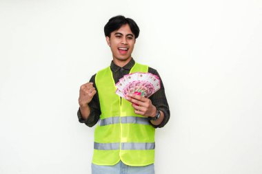 Asyalı mutlu inşaat işçisinin portresi, beyaz arka planda izole bir şekilde nakit tutarken başarıyı kutluyor.