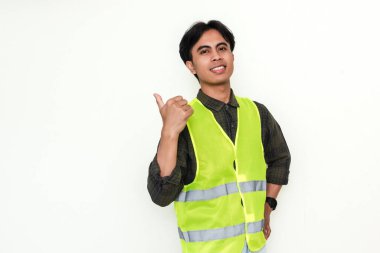 Gülümseyen Asyalı bir inşaat işçisinin portresi baş parmağıyla yanlamasına işaret ediyor, güvenlik teçhizatı takıyor, beyaz arka planda izole edilmiş. Reklamlar ve promosyon kullanımı için mükemmel