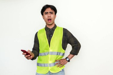 Güvenlik yeleği giymiş Asyalı inşaat işçisi elinde kızgın bir ifadeyle akıllı bir telefon tutuyor. Sektörde hayal kırıklığına uğramış bir anı gösteren izole bir portre.