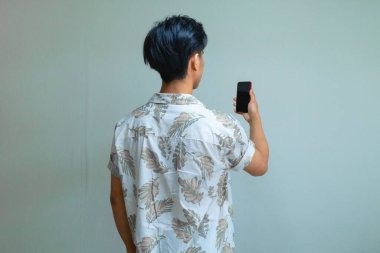 Yazlık giysiler giyen genç bir Asyalı 'nın arka plan portresi, arka plan temiz, reklam veya teknik promosyon için mükemmel bir akıllı telefon tutuyor.