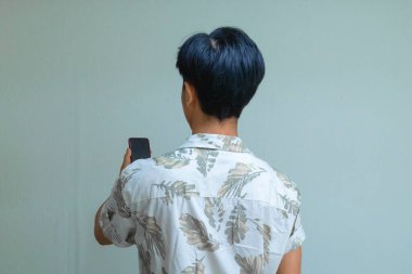 Yazlık giysiler giyen genç bir Asyalı 'nın arka plan portresi, arka plan temiz, reklam veya teknik promosyon için mükemmel bir akıllı telefon tutuyor.