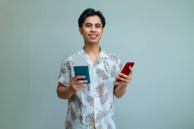 Pasaport ve uçak biletini elinde tutan mutlu, genç Asyalı bir adam. Akıllı telefon kullanıyor. Tatil ya da seyahat için heyecanlı.