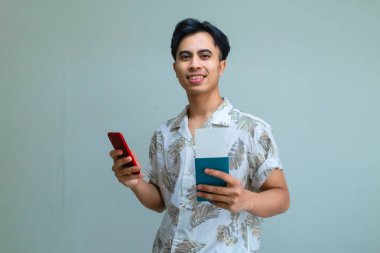 Pasaport ve uçak biletini elinde tutan mutlu, genç Asyalı bir adam. Akıllı telefon kullanıyor. Tatil ya da seyahat için heyecanlı.