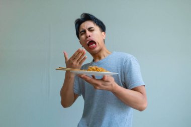 Bir tabak erişte yiyen genç Asyalı adam izole edilmiş arka planda komik bir yüz ifadesi sergiliyor, neşeli ve anlamlı bir yemek tepkisi yakalıyor.