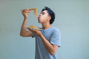 Neşeli bir ifadeyle bir tabak eriştenin keyfini çıkaran mutlu, genç Asyalı adam, temiz bir arka planda izole edilmiş, yemek, yaşam tarzı veya Güneydoğu Asya kültürü teması için mükemmel.