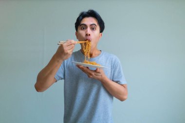 Neşeli bir ifadeyle bir tabak eriştenin keyfini çıkaran mutlu, genç Asyalı adam, temiz bir arka planda izole edilmiş, yemek, yaşam tarzı veya Güneydoğu Asya kültürü teması için mükemmel.