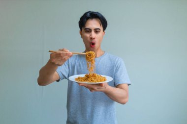 Temiz bir stüdyo arka planında çekilmiş bir tabak erişte yiyen Asyalı bir adamın komik ifadesi. Esprili ve doğal yemek anları reklamlar ya da yaşam tarzı içeriği için mükemmel