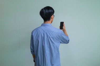 Akıllı telefon kullanan genç bir Asyalı 'nın arka plan portresi temiz bir arkaplanda duruyor. Basit, modern ve dijital yaşam tarzı veya teknoloji reklam temaları için uygun
