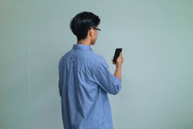 Akıllı telefon kullanan genç bir Asyalı 'nın arka plan portresi temiz bir arkaplanda duruyor. Basit, modern ve dijital yaşam tarzı veya teknoloji reklam temaları için uygun