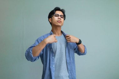 Tasmasını tutan Asyalı genç bir adamın portresi kibirli ve kibirli bir ifadeyle sade bir arka planda, özgüven ve cesur bir tutum sergiliyor.