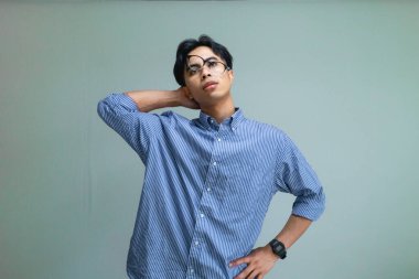 Stresli genç Asyalı bir adam, baskıya tepki verirken komik, berbat bir yüz ifadesi takınıyor, mizahi ve anlamlı bir ruh haliyle sade bir arka planda izole edilmiş.