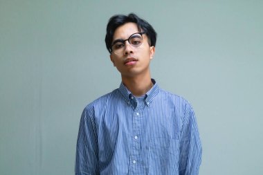 Stresli genç Asyalı bir adam, baskıya tepki verirken komik, berbat bir yüz ifadesi takınıyor, mizahi ve anlamlı bir ruh haliyle sade bir arka planda izole edilmiş.