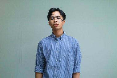 Stresli genç Asyalı bir adam, baskıya tepki verirken komik, berbat bir yüz ifadesi takınıyor, mizahi ve anlamlı bir ruh haliyle sade bir arka planda izole edilmiş.