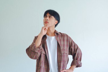 Asyalı bir adam çenesini tutuyor ve düşünceli bir ifadeyle yana bakıyor, sade bir arkaplanda izole edilmiş, reklamlar ve kavramlar için mükemmel..