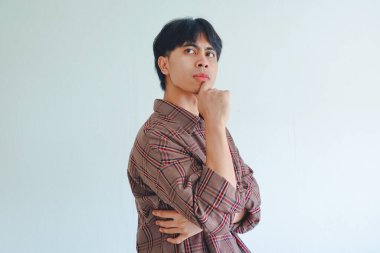 Asyalı bir adam çenesini tutuyor ve düşünceli bir ifadeyle yana bakıyor, sade bir arkaplanda izole edilmiş, reklamlar ve kavramlar için mükemmel..