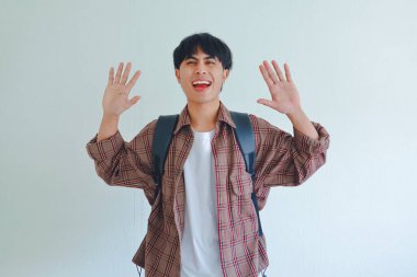 Merhaba! Sırt çantası takan gülümseyen erkek öğrencinin portresi. Beyaz arka planda izole bir şekilde arkadaşça bir yüz ifadesiyle merhaba demek için el sallıyor.