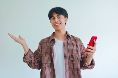 Gülümseyen Asyalı adam telefonu tutuyor ve fotokopi için avuçlarını açık tutuyor. Reklamcılık ya da beyaz arka planda promosyon konsepti için mükemmel.