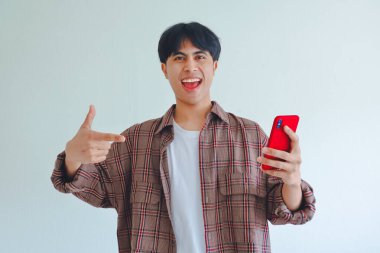 Beyaz arka planda heyecanlı bir yüzü olan akıllı telefonu işaret eden mutlu Asyalı adam teknoloji, promosyon ya da yaşam tarzı teması için mükemmel.