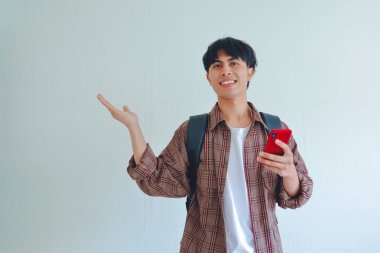 Sırt çantalı, cep telefonlu mutlu bir üniversite öğrencisi, avuç içi açık, reklam alanı sunuyor, beyaz arka planda izole edilmiş.