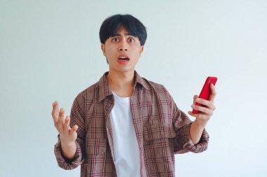 Şok olmuş Asyalı adam akıllı telefona geniş gözlerle ve şaşırmış bir ifadeyle bakıyor.