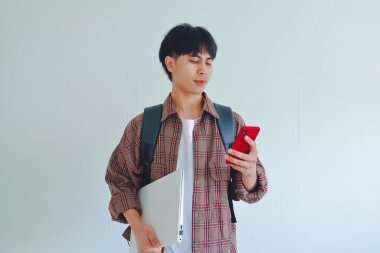 Sırt çantalı ve akıllı telefon kullanan Asyalı bir erkek öğrencinin portresi, beyaz arka plan, eğitim ve teknoloji kavramına izole edilmiş.