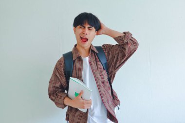 Sırt çantası geniş olan yorgun bir üniversite öğrencisi. Uykulu ve bitkin görünüyor. Arka planda izole edilmiş..