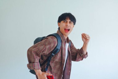 Sırt çantalı genç Asyalı bir erkek öğrenci, enerjik bir ifade takınıyor, beyaz arka planda izole edilmiş, eğitim veya yaşam tarzı konsepti için mükemmel.