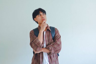 Sırt çantası taşıyan bir erkek üniversite öğrencisi kafasını kaldırıp düşünceli bir ifade sergiliyor.