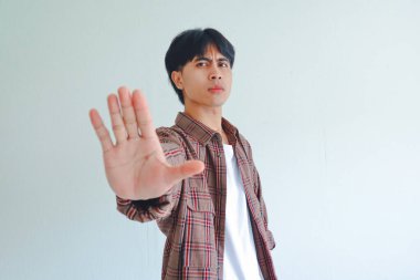 Ciddi genç Asyalı adam, beyaz arka planda izole bir şekilde el hareketi yapıyor. Uyarı ya da sert bir ifadeyle reddediyor.