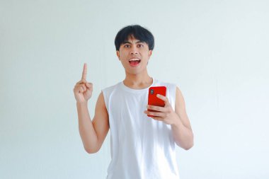 Mutlu Güneydoğu Asyalı adamın portresi, elinde akıllı telefon, heyecanla gülümsüyor, beyaz arka planda izole edilmiş, başarı kavramı, sürpriz veya iyi haber.