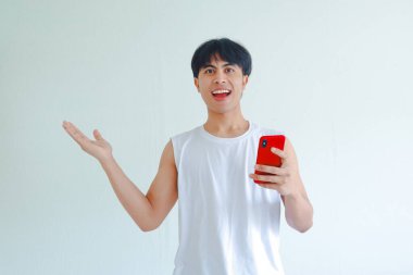 Heyecanlı Asyalı genç adam elinde akıllı telefon, neşeli yüz ifadesi, beyaza izole edilmiş, uygulamayı veya ürünü destekleyen, açık avuç içi ile kopyalama alanını işaret ediyor.