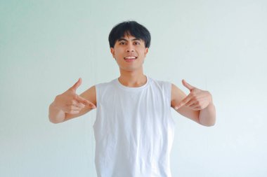 Spor elbiseli mutlu bir Asyalı adamın portresi iki eliyle aşağıya bakıyor ve neşeyle gülümsüyor, beyaz arka planda izole edilmiş, fitness reklamları ve promosyonlar için mükemmel.