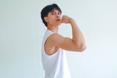Jimnastik salonundaki kendine güvenen genç Asyalı adam kollarını esnetip ciddi bir ifade takınıyor, kameraya güç ve güç gösteriyor, beyaz arka planda izole edilmiş, fitness ve egzersiz konsepti.