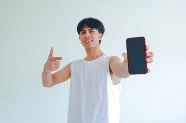 Boş cep telefonu ekranını işaret ederken gülümseyen spor kıyafetli mutlu bir Asyalı. Beyaz arka planda izole edilmiş. Fitness uygulaması, promosyon ya da reklam modeli için mükemmel.