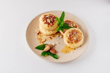 Lezzetli kahvaltı - süzme peynir krep, cheesecakes, badem, nane ve akçaağaç şurubu ile süzme peynir krep bir bej plaka. Beyaz arka planda faydalı tatlı (izole)