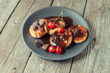 Gurme kahvaltı - süzme peynir krep, peynir kek, kiraz ve kahverengi bir tabakta çikolata ile süzme peynir krep. Rustik tarzda ahşap bir masada faydalı tatlı. Seçici odaklama.