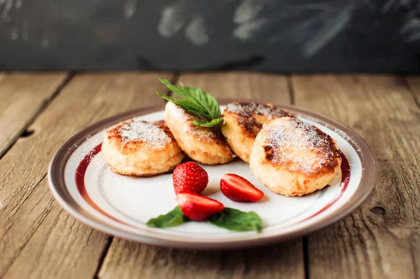 Gurme kahvaltı - süzme peynir krep, cheesecakes, çilek, nane ve beyaz bir tabakta pudra şekeri ile süzme peynir krep. Rustik tarzda ahşap bir masada faydalı tatlı. Seçici odaklama.