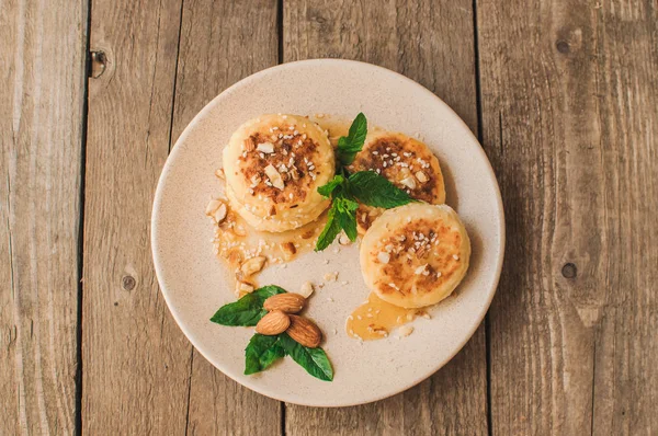 Delicious breakfast - cottage cheese pancakes, cheesecakes, cottage cheese pancakes with almonds, mint and maple syrup in a beige plate. Useful dessert on a wooden table in rustic style. Selective focus.copy space.