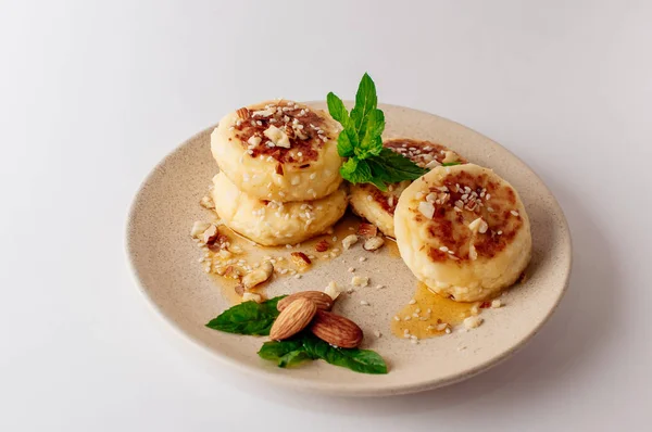 Delicious breakfast - cottage cheese pancakes, cheesecakes, cottage cheese pancakes with almonds, mint and maple syrup in a beige plate. Useful dessert on white background (isolate)