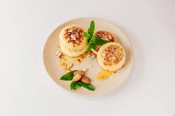 Delicious breakfast - cottage cheese pancakes, cheesecakes, cottage cheese pancakes with almonds, mint and maple syrup in a beige plate. Useful dessert on white background (isolate)