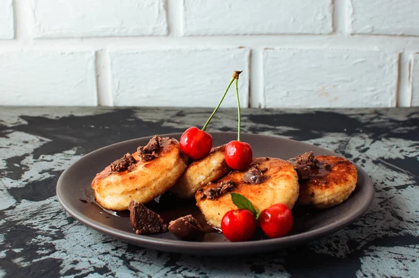 Kahvaltı Gıda Lezzetli Kavramı. Cheesecakes, cheesecakes, kiraz ve çikolata beton bir masa ve beyaz bir tuğla duvar siyah bir arka plan ile süzme peynir krep. Close-up.Sağlıklı gıda