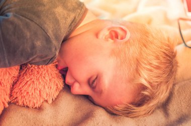 Sevimli bir 5 yaşındaki çocuk oyundan sonra yorgun var ve bir oyuncak ayı ile kanepede öğleden sonra uykuya daldı. Gün batımında uyuyan bir bebeğin portresi. Dinlenme kavramı.