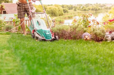 Doğal arka plan. Yazın bir çiçek bahçesinin yanındaki bahçesinde çim biçme makinesi olan bir adam. Yan görüş, yatay. Tasarım, doğa ve peyzaj kavramı.