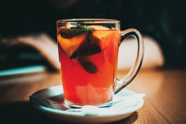 Şeffaf fincanda meyve çayı, limon dilimleri, portakal ve nane. Kafedeki ahşap bir masanın üzerinde bir fincan çay var. Sonbaharda sıcacık zaman kavramı.