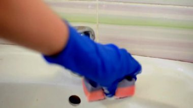 Mavi lateks eldivenli kadın eller lavaboyu havluyla ovalıyor. Lavabonun etrafında bir sürü köpük var. Banyoyu temiz tutma konsepti.