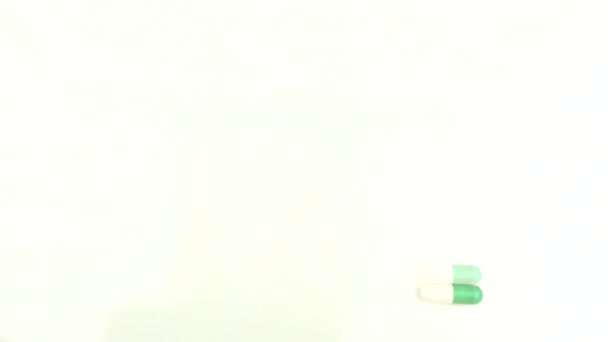 Biało-zielone tabletki i witaminy toczą się na białym tle. — Wideo stockowe