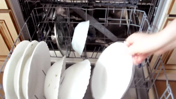 Lány tesz piszkos edények és evőeszközök egy modern mosogatógép evés után a konyhában. Mosogatógép piszkos edényekkel és csészealjjal. — Stock videók