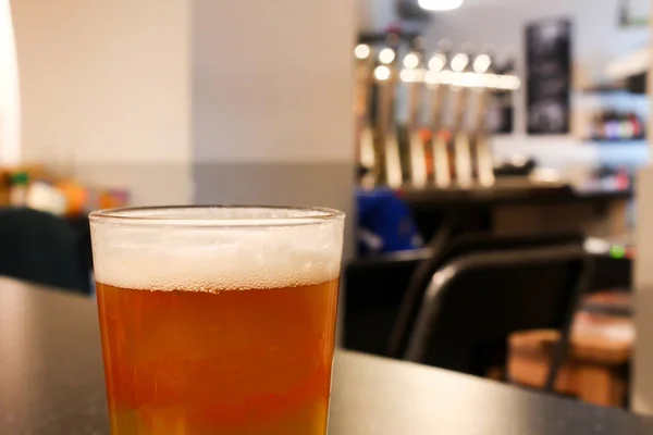 Full glass of light orange juicy tasty beer in a cozy light craft beer bar with shiny silver beer taps and grey wall background