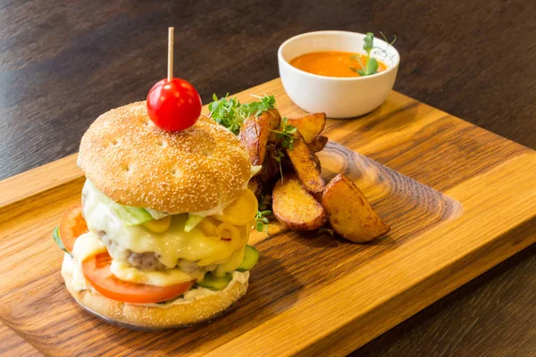 Delicious burger with meat, vegetables, potatoes and orange sauce on a wooden platter background
