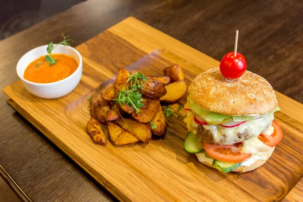 Delicious burger with meat, vegetables, potatoes and orange sauce on a wooden platter background